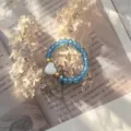 Detail of blue crystal faceted bead elastic ring with a white heart-shaped shell - Stretch / Aqua