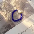 Close-up of a blue crystal bead ring with a white shell heart charm on vintage paper. - Stretch / Blue