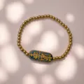 Detaillierte Ansicht des eleganten goldverzierten Runenanhängers am goldenen Perlenarmband - Talisman-blue
