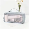 Dettaglio della borsa porta asciugacapelli grigia in rete con all'interno un phon rosa. - Blu
