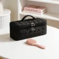Detailed view of black heart-quilted makeup bag with pearl zippers on white table. - Black Heart