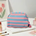 Close-up of a striped shell-shaped cosmetic bag with pink and blue colors and pom-poms - Blue Stripe