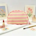Detail view of pink and yellow striped canvas makeup bag with soft pom-pom zipper pull - Pink Stripe