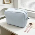 Primer plano de neceser waffle azul claro sobre un tocador blanco con brochas de maquillaje. - Azul claro