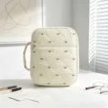 Primer plano de una bolsa acolchada crema con bordado de lazos sobre un escritorio. - Beige