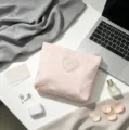 Macro detail of a soft pink lace bow cosmetic bag on a stylish lifestyle desk setup. - Pink