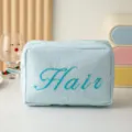 Gros plan d'une trousse de toilette rayée bleu clair avec broderie 'Hair' devant - Style Brodé Hair / Bleu lac