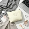 Elegant cream makeup bag with heart embroidery and bow detail shown in lifestyle setting - Yellow