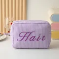 Vue détaillée montrant la texture et la broderie Hair sur une trousse de maquillage à rayures - Style Brodé Hair / Violet