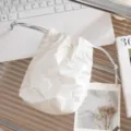 Detalle de una bolsa de maquillaje blanca acolchada con lazos y cordón ajustable. - Patrón de Lazo / Beige
