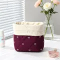 Detail view of a quilted burgundy drawstring makeup bag with white bow embroidery - Angola Red