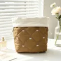 Detail of a brown quilted drawstring makeup bag with white bow embroidery on a desk. - Caramel color
