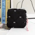 Close-up of black quilted pouch with white bow patterns on a white table with books. - Black