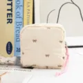 Close-up of cream quilted toiletry bag featuring embroidered bows and a pink zipper pull - Beige