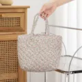 Primer plano de un neceser acolchado con estampado floral sujetado por una mano elegante - Tamaño: 27*10*18.cm / Rosa Floral