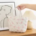 Primer plano de un neceser acolchado blanco con patrones de lazos rosas sostenido a mano - Tamaño: 27*10*18.cm / Blanco con lazo rosa