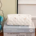 Close-up of a white quilted cotton pouch with delicate floral patterns on books. - Pencil Case
