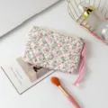 Detalle de un neceser acolchado de flores con correa rosa sobre un escritorio blanco. - Rosa Floral