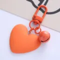 Close-up detail van een feloranje hartvormige sleutelhanger met een klein belletje - Oranje