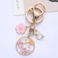 Close-up detail of cute white bunny and pink sakura enamel charms on a gold-tone alloy keychain - Moon Rabbit
