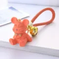 Close-up of cute resin lucky bear keychain with gold bell and orange woven strap - Orange