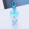 Detail view of a cute iridescent blue acrylic bear keychain with a stylish bow decoration - Blue