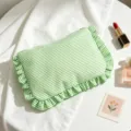 Close-up of green striped seersucker cosmetic bag with ruffles and makeup props - Green