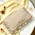 Close-up of stylish striped seersucker makeup bag with ruffle trim and zipper detail. - Khaki