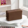 Detailopname van een bruine make-up tas met wafeltextuur op een witte standaard - koffiekleur