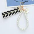 Detailed view of woven strap keychain with white pearl loop and gold shell charm. - Black