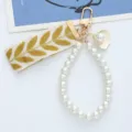 Detail view of pearl bead lanyard and embroidered ribbon on gold keychain - Tan