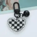Macro detail of a heart-shaped acrylic keychain with checkered pattern and black bell. - Black Checkerboard Heart