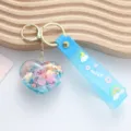 Close-up detail of a blue heart-shaped quicksand keychain with seashells and glitter - Blue