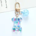 Detail view of a cute transparent acrylic bear keychain with vibrant colorful splatter patterns. - Blue