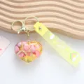Detail of heart-shaped resin keychain filled with shells and glitter on yellow strap - Yellow
