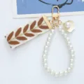 Close-up detail of an elegant pearl bead keychain featuring a brown leaf-patterned ribbon - Brown