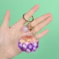Detailed view of a purple seashell keychain with glitter quicksand effect held in hand. - Shell Decoration / Shell Purple