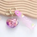 Close-up of a pink heart quicksand keychain with shell sequins and 'wish' strap. - Purple