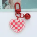Macro view of a red checkered acrylic heart keychain with a glossy bell pendant. - Red Plaid Heart