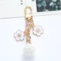 Detail showing the white enamel cherry blossom charms and fluffy pom-pom on gold keychain - White