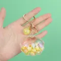 Close-up detail of a transparent shell keychain filled with liquid and colorful charms - Shell Decoration / Shell Yellow