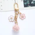 Close-up of pink cherry blossom and pom-pom keychain with gold-tone hardware - Pink