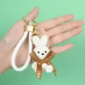 Close-up of a white resin rabbit keychain with woven texture and brown ribbon - White