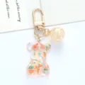 Close-up of a colorful acrylic bear keychain with gold metal lobster clasp and glittery bead - Orange