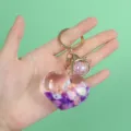Detail view of heart-shaped liquid keychain with shells and purple quicksand glitter. - Purple Heart