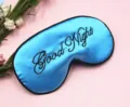 Close-up detail of a blue satin sleep eye mask with black Good Night embroidery - Blue