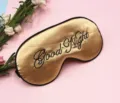 Close-up of gold satin sleep mask with black Good Night embroidery on pink background - Gold