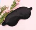 Close-up of black satin sleep mask with elastic strap on a pink floral background. - Black