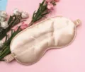 Close-up of champagne silk sleep mask with elastic strap on pink floral background - Champagne
