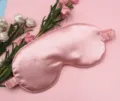 Detailed view of a soft pink silk-like sleep eye mask surrounded by decorative roses - Fresh Pink